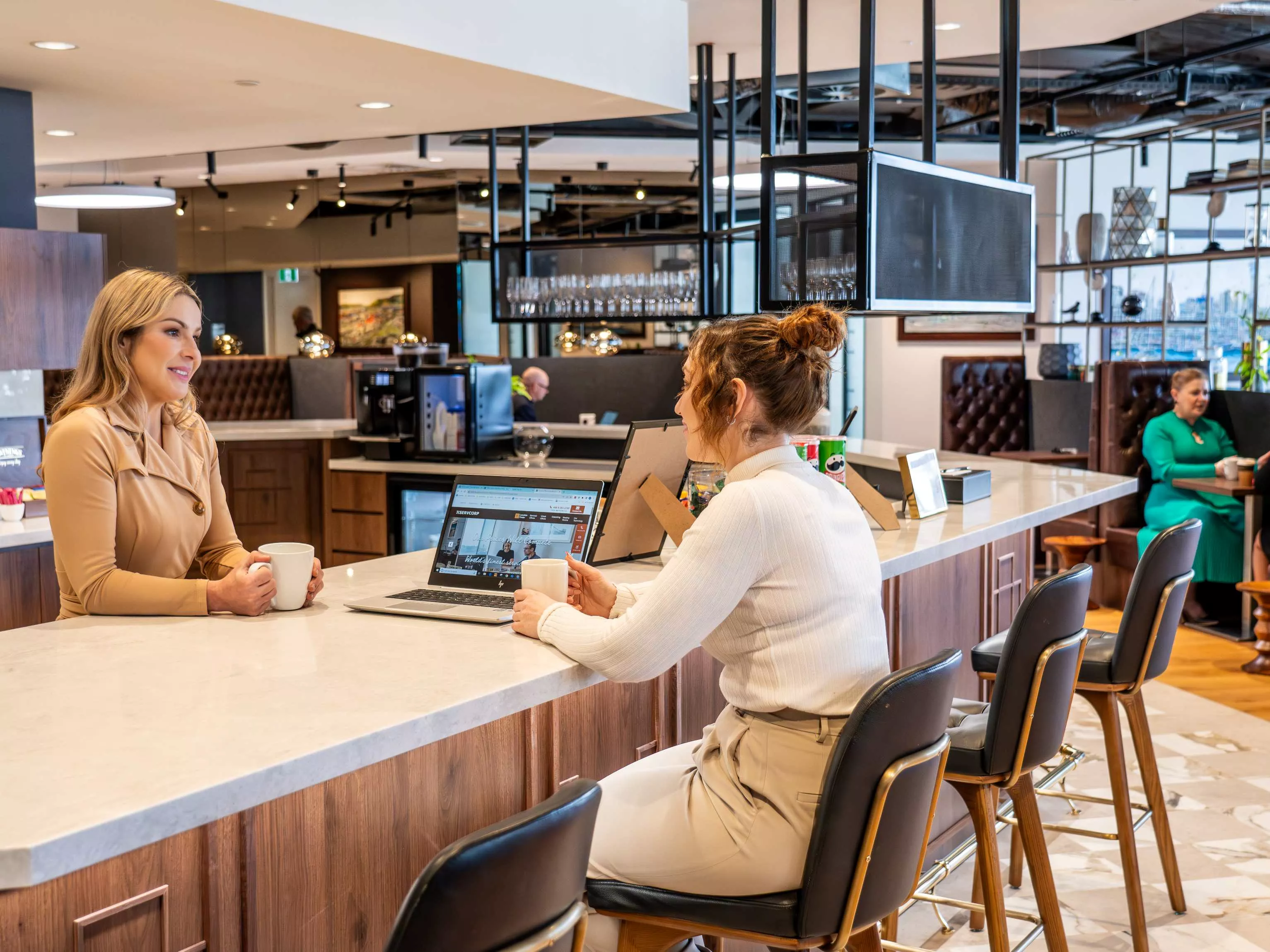 Clients enjoying the fully stocked kitchen and coffee break with surrounding booths in the coworking space of Servcorp 139 Quay Street, Auckland